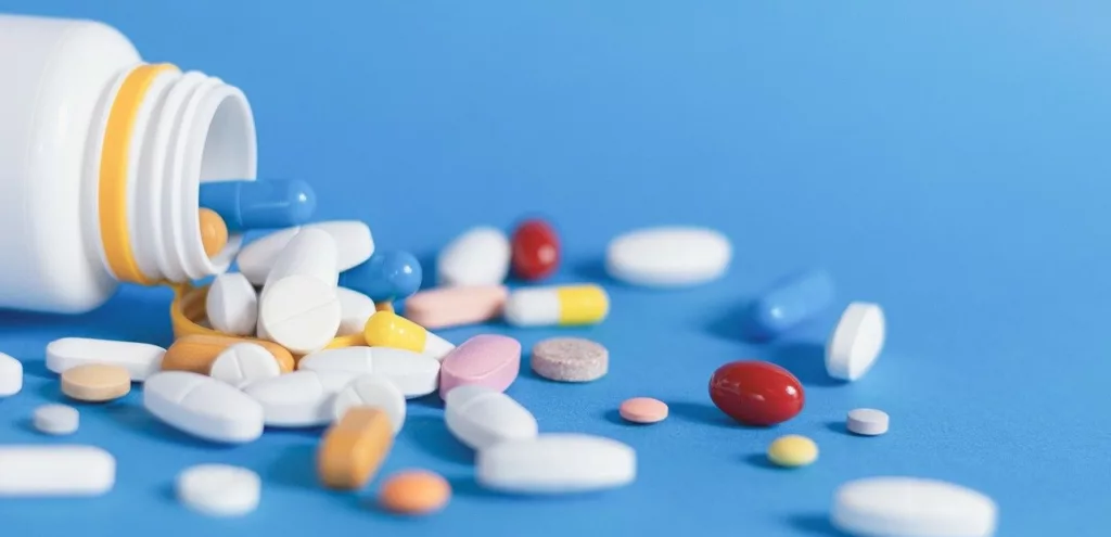 different colored pills spilling out from a white pill bottle